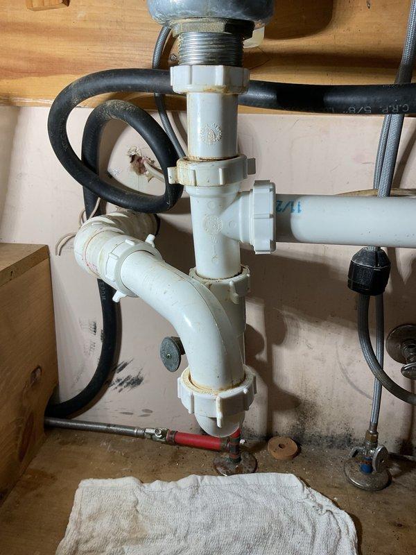 Installed new InSinkErator 777SS garbage disposal unit under kitchen sink, including complete drain assembly with white PVC P-trap configuration, compression fittings, and chrome tailpiece connections. Connected discharge plumbing with proper sealing at all joints, installed water supply shutoff valve with red handle and flexible supply line, and secured all rubber hoses with metal hose clamps to ensure leak-free operation.
