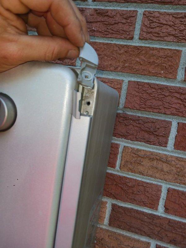 Accessed and inspected plumbing valve assembly through existing wall opening in bathroom fixture area. Valve assembly showed evidence of previous water activity with visible staining and mineral deposits on surrounding surfaces. Examined brass shut-off valve with dual blue-handled connections and verified accessibility for future maintenance requirements. External hose bib or water connection point on brick exterior was also inspected to ensure proper mounting and operational integrity of the metallic access panel and hinge assembly.