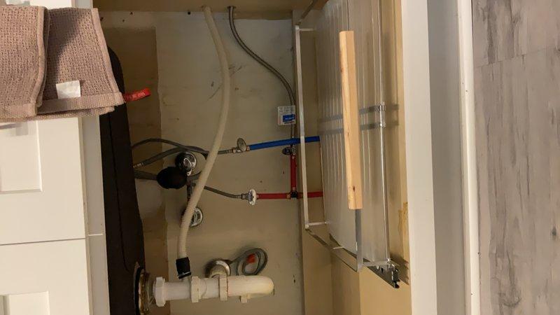 Completed installation of PEX plumbing system in utility room, including hot and cold water supply lines with proper color-coded piping (blue for cold, red for hot). Secured all pipes to structural joists using copper clamps and brackets, ensuring proper support and code compliance. Configured white PVC drain piping with appropriate fittings and connections to washing machine appliance. All plumbing components were properly fastened to wood framing with metal brackets, and connections were completed with standard fittings where PEX lines interface with existing plumbing infrastructure.