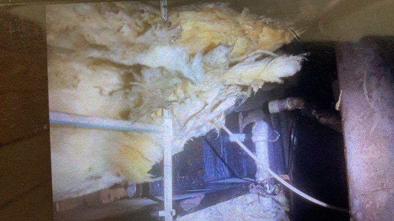 Performed inspection and documentation of attic HVAC system and insulation conditions. Photographed existing ductwork installation, noting white PVC piping runs and fiberglass insulation placement throughout the attic space. Documented current state of mechanical systems including metal ductwork secured with plastic support straps, exposed wooden framing, and utility line routing for maintenance records.