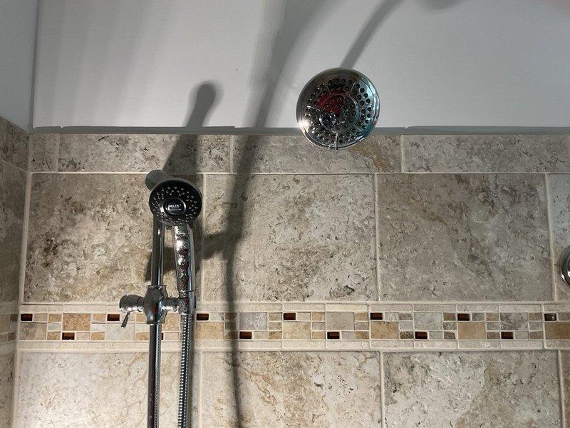 Installed new shower fixtures including a chrome wall-mounted showerhead and handheld shower unit with sliding bar in bathroom. Replaced existing shower arm and ensured proper mounting and secure connections for all components