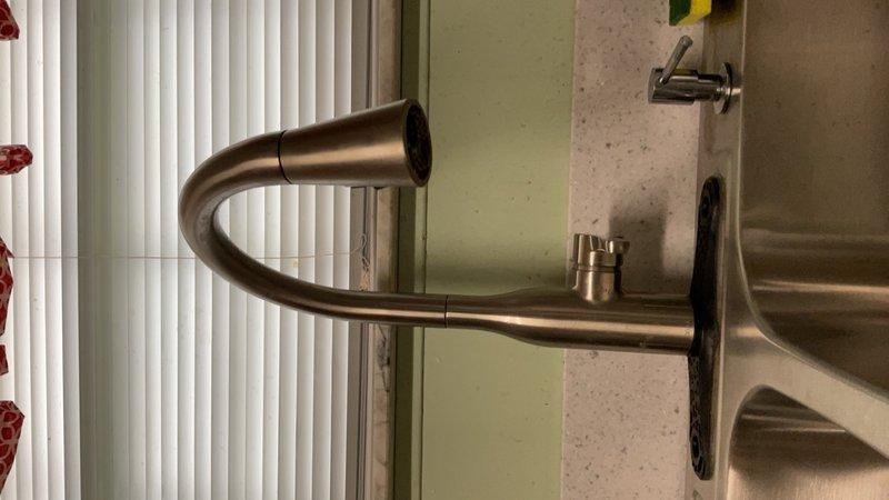 # Faucet and Under-Sink Plumbing Installation

Completed installation of a modern kitchen faucet with pull-down sprayer functionality, featuring a brushed nickel/bronze finish with distinctive U-shaped design. The faucet was mounted to a stainless steel sink basin with proper sealing and alignment to the existing countertop configuration.

Performed comprehensive under-sink plumbing work including installation and connection of water supply lines using brass valve assemblies and PVC drainage piping. Configured supply lines with appropriate shut-off valves for both hot and cold water connections. Installed flexible supply hoses with proper routing to prevent kinking or strain on connections. Ensured all PVC drain fittings were properly assembled with correct slope for drainage efficiency.

Verified all connections for leaks, tested faucet operation including sprayer function, and confirmed proper water flow and drainage performance.