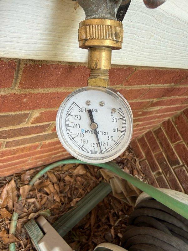 Performed water pressure testing at exterior hose bib connection point using calibrated pressure gauge to assess system performance. Conducted site inspection of recent utility access work in residential backyard area, documenting ground conditions and verifying proper installation of underground access panel near HVAC equipment location.