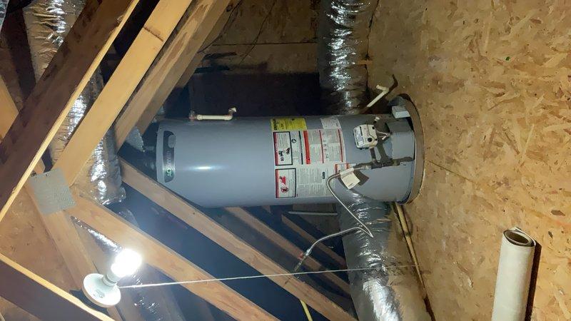 Performed inspection and documentation of water heater installation in attic space. Unit observed to be properly mounted on wooden support platform with appropriate copper piping connections at top of tank. Verified presence of required safety labels and EnergyGuide documentation affixed to exterior of tank. Documented existing installation conditions including proximity to ductwork, adequate clearances within attic framing, and accessibility for future maintenance requirements.