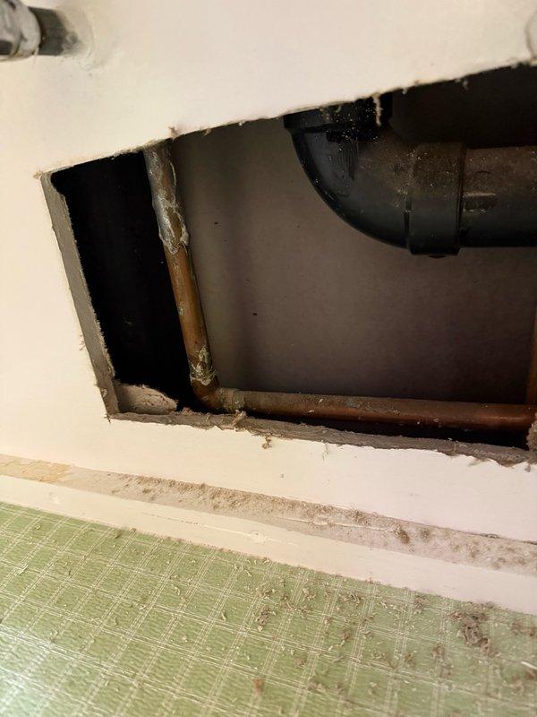 # Plumbing System Access and Inspection

Created access opening in wall to expose and inspect plumbing infrastructure. Documented condition of existing drainage and water supply lines, including modern PVC drain piping and aging copper supply pipes showing corrosion and mineral deposits. Identified areas of concern with oxidized copper piping and potential deterioration requiring monitoring or future replacement.