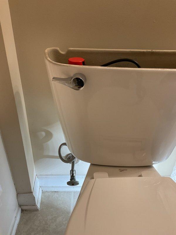 Responded to service call for toilet maintenance. Upon arrival, removed tank lid to inspect internal flush mechanism components. Found discolored water in tank indicating mineral deposits and potential supply line issues. Examined fill valve assembly with red adjustment cap, overflow tube with rubber flapper, and float mechanism. Inspected flexible water supply line connection and chrome shut-off valve at wall mounting point. Assessed Mansfield brand toilet for proper operation and identified need for water quality evaluation due to rust staining or mineral buildup in tank. Documented fixture condition and internal component status through photographs for service records.