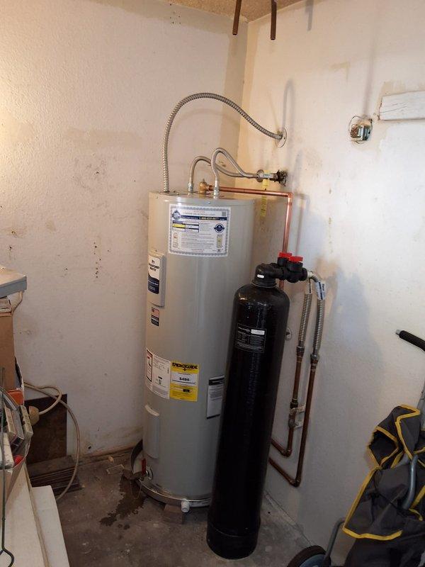Completed preventative replacement of 13-year-old residential electric water heater with new 50-gallon RE350S6 model unit. Removed existing 4-foot tall electric water heater from utility closet, installed replacement unit with proper wall strapping, connected flexible braided supply lines, integrated with existing water treatment system, and verified all plumbing connections and electrical components for proper operation.