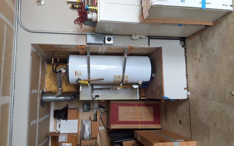 Completed residential water heater replacement with installation of 50-gallon natural gas unit in utility room. Installed additional expansion tank and drain pan for code compliance and system protection. Configured all copper piping connections with brass fittings, secured unit to wooden frame support structure, and verified proper venting through flexible aluminum duct system with appropriate wall penetrations and insulation.