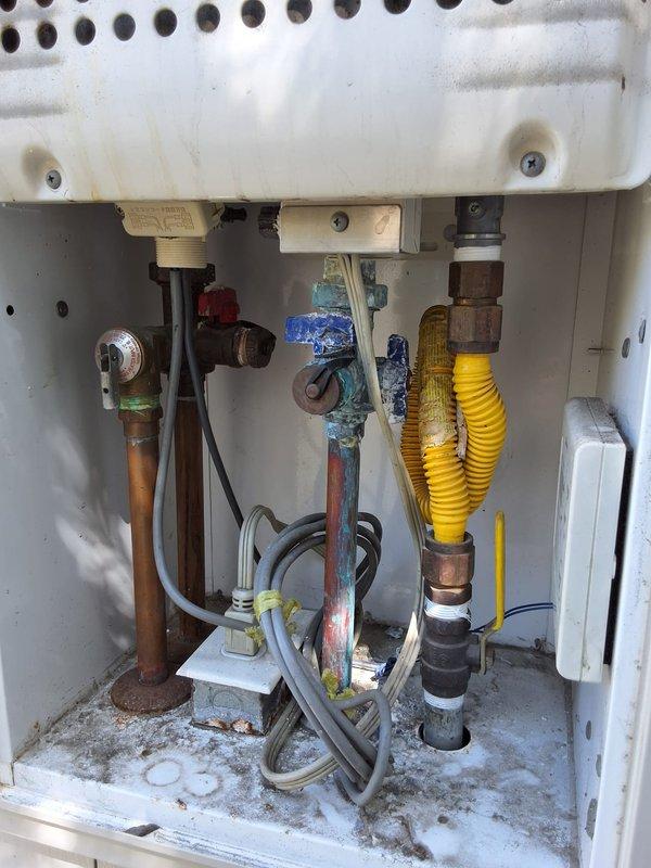 Performed preventive maintenance inspection on two tankless water heater systems at residential property. Evaluated plumbing connections, isolation valves, and gas supply lines, noting visible corrosion on copper piping, mineral deposits in equipment compartment, and aging valve components. Documented system condition with photographs showing corrugated gas flex line, shut-off valves, and pressure relief connections requiring monitoring for future service needs.