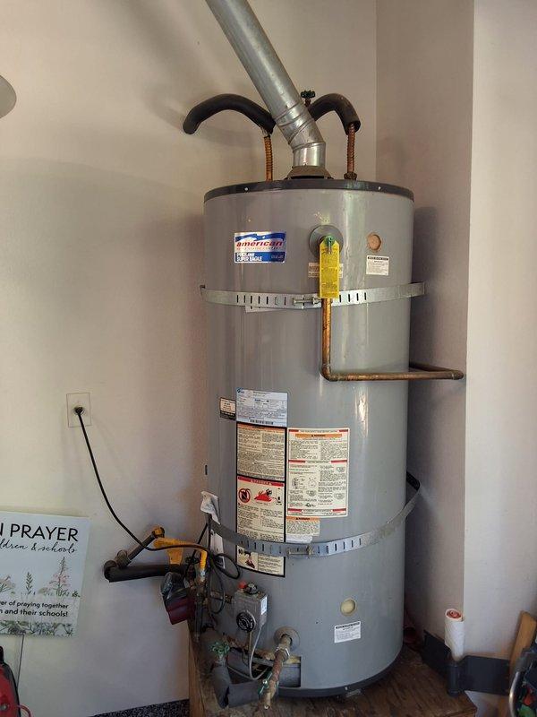 Responded to service call for leaking water heater. Upon inspection, found 21+ year old American brand residential gas water heater showing signs of age and active leak. Unit installed on wooden platform in utility closet with standard gas, water, and electrical connections. Evaluated existing installation including flexible gas line, copper water piping, pressure relief valve, and venting system. Discussed multiple replacement options with customer including traditional tank-style water heater, tankless water heater conversion, and heat pump water heater conversion. Provided estimates for like-for-like replacement as well as upgraded efficiency options. Reviewed permit requirements for replacement work. Documented existing installation with photographs showing current equipment condition, piping configuration, gas connections, and available space constraints. Customer to review options and schedule replacement service. Available payment methods confirmed.