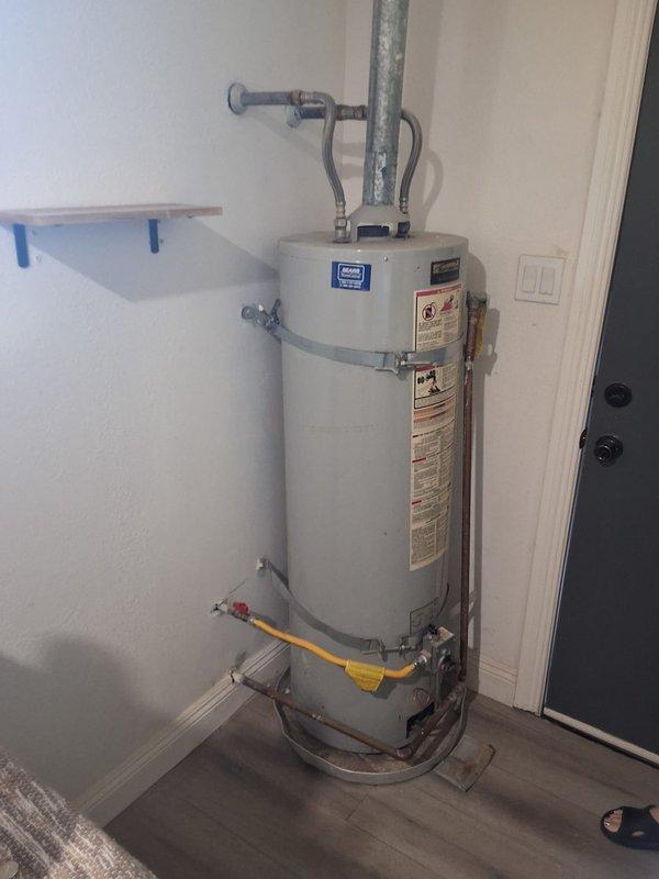 Replaced non-functioning 2014 Kenmore water heater (Model 153.3324632) with new 40-gallon gas water heater in residential utility room. Installation included proper venting with gray metal exhaust piping, yellow flexible gas line connection, water supply line hookups, and wall-mounted safety straps for seismic stability. Customer was advised of permitting requirements and provided cost estimate range for the complete replacement.