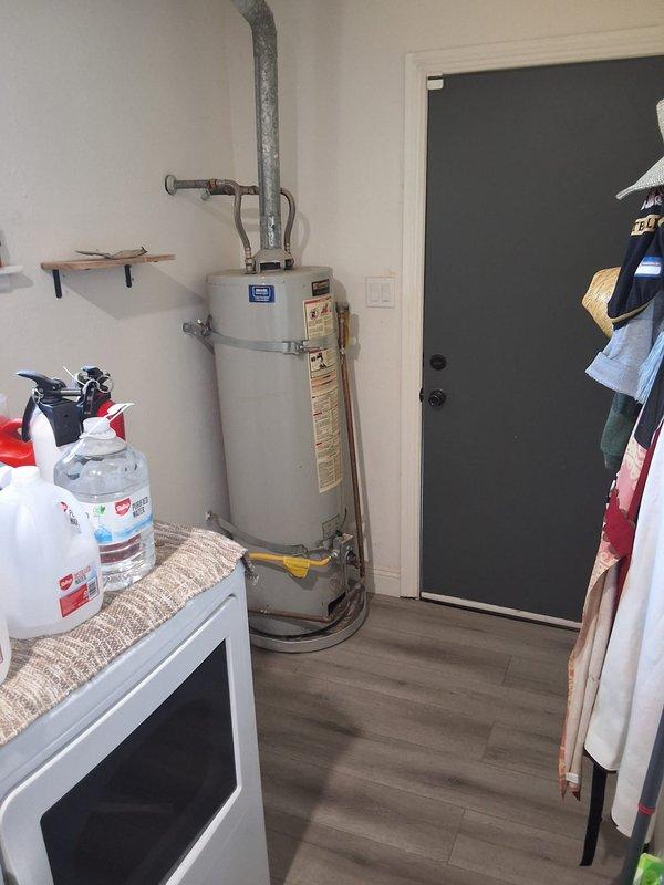 Replaced non-functioning 2014 Kenmore water heater (Model 153.3324632) with new 40-gallon gas water heater in residential utility room. Installation included proper venting with gray metal exhaust piping, yellow flexible gas line connection, water supply line hookups, and wall-mounted safety straps for seismic stability. Customer was advised of permitting requirements and provided cost estimate range for the complete replacement.