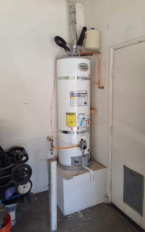 Replaced existing 40-gallon gas water heater from 2016 with new American Standard 40-gallon gas unit. Installed new expansion tank, connected copper supply lines, and verified proper pressure relief valve operation with gauge reading approximately 100 PSI. Secured unit with seismic restraint straps per code requirements, mounted on elevated platform with PVC drainage, and discussed permit requirements with property owner.