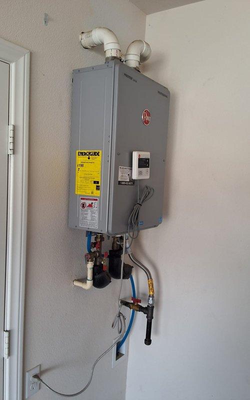 Responded to service call for tankless gas water heater that has not been maintained in over five years. Conducted thorough inspection of existing Rheem tankless unit and determined that due to lack of service history and current condition, replacement is recommended over repair. Evaluated installation location, existing venting configuration with dual exhaust pipes through exterior wall, and current gas and water line connections. Provided estimate for complete tankless water heater replacement including new unit installation, necessary plumbing modifications, and gas line work. Advised that municipal permit will be required for replacement and documented existing installation with photographs for estimate preparation.