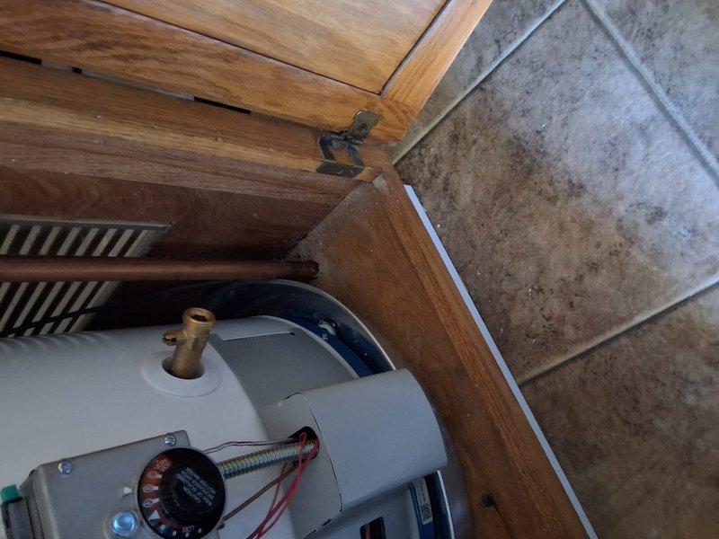 Responded to inspector callback for water heater installation model GN40T1-3-6. Documented T&P relief valve discharge line routing and termination point with photographs per inspector's requirements. Photos captured T&P line path from water heater through wooden cabinet enclosure and exterior termination beneath deck structure, showing proper drainage to landscaped area with appropriate air gap compliance.