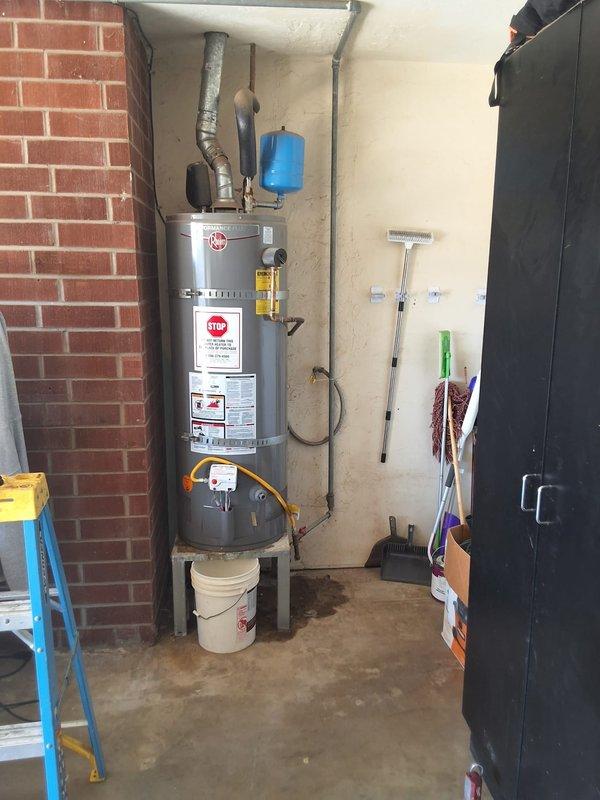 Performed inspection and estimate on leaking 50-gallon propane water heater in utility room. Upon arrival, observed aging cylindrical water heater with visible corrosion on copper plumbing connections, including green patina and oxidation on supply lines and vertical piping. Blue expansion tank mounted above unit showed signs of age. Documented equipment condition with photographs showing corroded copper piping, discolored flooring beneath unit indicating previous water leakage, and overall deterioration of plumbing infrastructure. Discussed permit requirements for replacement work and available payment options including credit card and check. Provided free estimate for complete water heater replacement with new 50-gallon propane unit.