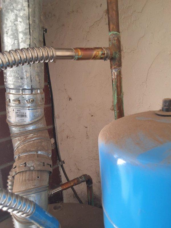 Performed inspection and estimate on leaking 50-gallon propane water heater in utility room. Upon arrival, observed aging cylindrical water heater with visible corrosion on copper plumbing connections, including green patina and oxidation on supply lines and vertical piping. Blue expansion tank mounted above unit showed signs of age. Documented equipment condition with photographs showing corroded copper piping, discolored flooring beneath unit indicating previous water leakage, and overall deterioration of plumbing infrastructure. Discussed permit requirements for replacement work and available payment options including credit card and check. Provided free estimate for complete water heater replacement with new 50-gallon propane unit.