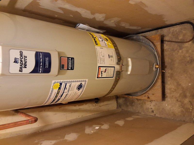 Completed full residential water heater replacement at rental property as preventative measure in advance of heat pump mandate regulations. Removed existing Bradford White URG140 40-gallon gas water heater (S#WE45140214) and installed new American Standard 40-gallon gas water heater. Installation included proper mounting with seismic strapping brackets for code compliance, connection of gas supply line via black pipe, copper water supply piping connections, temperature and pressure relief valve installation with discharge piping, and electrical connections. Unit secured to wooden platform base on concrete floor in basement utility area. All connections tested and verified for proper operation and safety. Municipal permit obtained and work performed to current building code standards.