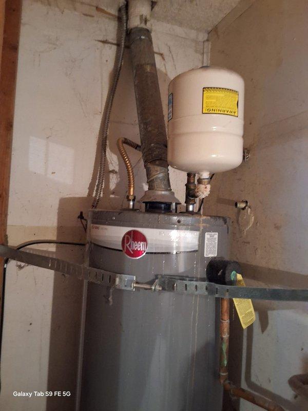 Replaced a leaking 40-gallon propane water heater (PROG40-32P) that was experiencing failure from the top of the tank. Installed new Rheem 40-gallon LP gas water heater (model LGSN40T1-3-6LP) with expansion tank, new venting system including vertical black exhaust pipe, copper supply line connections, and flexible braided hose connections. Unit was positioned in basement utility area and all plumbing connections were completed to code specifications, with county permit requirements advised for final approval.