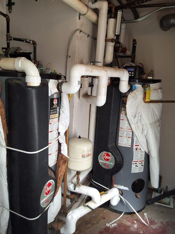 Inspected two approximately 12-year-old Rheem Commercial GHE100ES-400 water heaters in the utility room and documented their condition, including aged and stained piping insulation, discolored PVC runs, loose wrap, and general wear at the units and associated plumbing. Units are at end of service life and recommended for replacement; site measurements and photos were gathered to support a replacement bid, with installation to be scheduled on-site for the earliest available window.