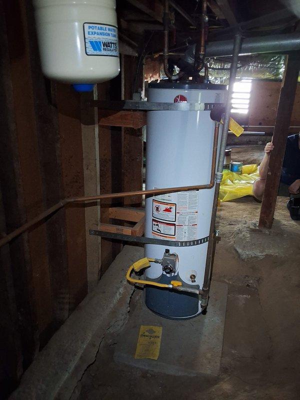 Inspected existing 40-gallon gas water heater in crawlspace installation, noting seismic strapping, flexible gas connector, copper supply piping, thermal expansion tank, and a cracked concrete pad beneath the unit. Provided replacement options for standard tank, tankless, and heat pump water heaters, and discussed permit requirements and payment options with the homeowner.