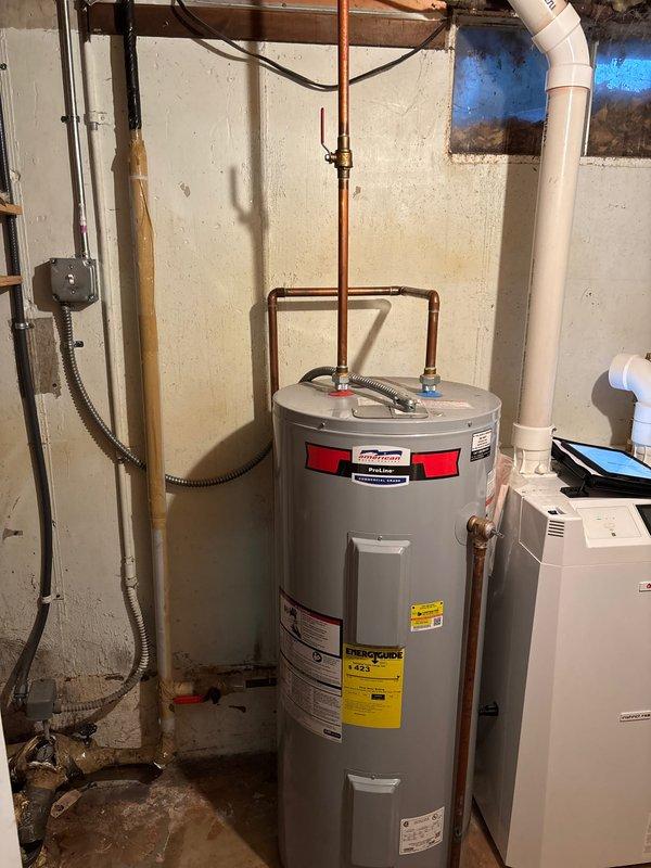 Performed comprehensive assessment of existing water heater installation in response to inadequate hot water capacity for household demand. Inspected aging water heater unit located in basement utility area, noting gray cylindrical tank with copper piping connections, brass fittings, and loop configuration at top of unit. Evaluated current system capacity relative to home age (circa 1970) and occupant usage patterns indicating hot water depletion after multiple consecutive showers. Documented equipment condition through photographic records showing water heater positioning against concrete block wall with associated plumbing infrastructure, electrical conduit connections, and visible warning labels. Observed moisture staining on concrete floor at base of unit and general signs of system age. Assessed copper supply lines, red-handled ball valve, brass fittings, and overall plumbing configuration. Reviewed manufacturer specifications on unit labeling and determined replacement recommenda