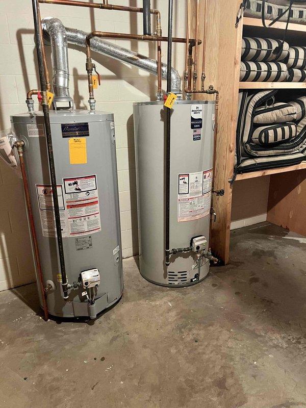 Responded to service call for water heater leaking onto floor. Upon arrival, found two water heaters installed side by side in basement utility area on concrete floor with visible water staining and discoloration indicating active or recent leakage. Conducted thorough visual inspection of both units, including examination of tank exteriors, plumbing connections, copper supply lines, brass fittings, valves, and exhaust venting. Inspected all pipe joints and connections for signs of corrosion, mineral deposits, or active leaks. Assessed age and condition of both water heaters based on manufacturer labels and overall wear patterns. Documented existing installation configuration including copper piping network, insulated lines, and connection points. Photographed units and surrounding area showing tank conditions, plumbing connections, floor staining, and mechanical room setup for service records. Provided assessment findings and recommendations to customer regarding unit age, leak source 