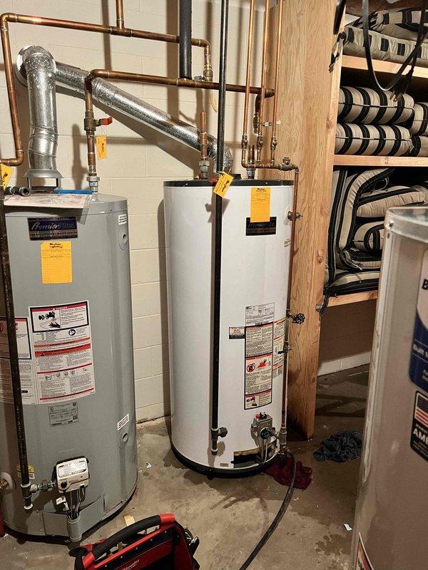 Responded to service call for water heater leaking onto floor. Upon arrival, found two water heaters installed side by side in basement utility area on concrete floor with visible water staining and discoloration indicating active or recent leakage. Conducted thorough visual inspection of both units, including examination of tank exteriors, plumbing connections, copper supply lines, brass fittings, valves, and exhaust venting. Inspected all pipe joints and connections for signs of corrosion, mineral deposits, or active leaks. Assessed age and condition of both water heaters based on manufacturer labels and overall wear patterns. Documented existing installation configuration including copper piping network, insulated lines, and connection points. Photographed units and surrounding area showing tank conditions, plumbing connections, floor staining, and mechanical room setup for service records. Provided assessment findings and recommendations to customer regarding unit age, leak source 