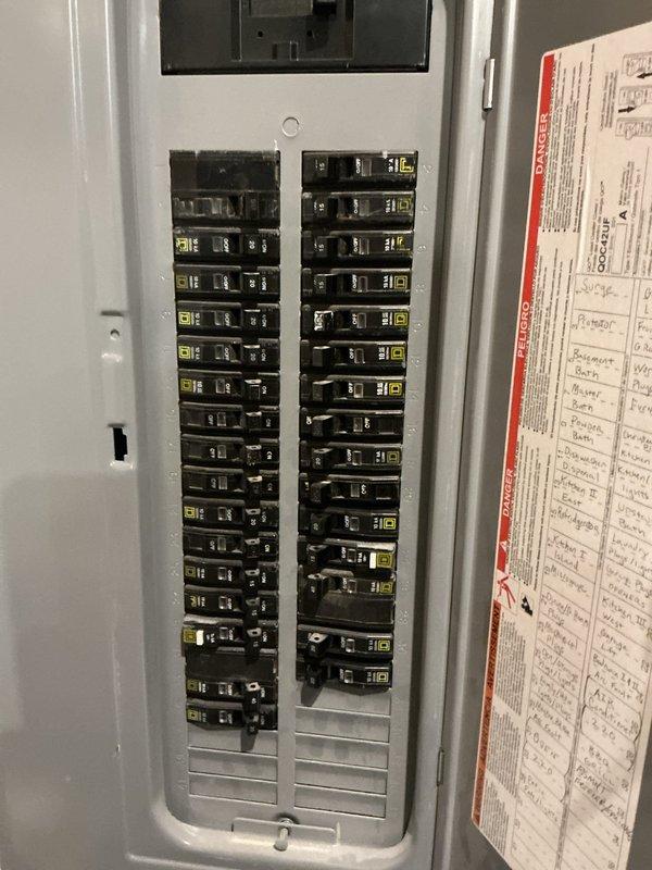 Conducted on-site evaluation for standby Generac generator installation. Documented existing electrical infrastructure including main service panel with Square D circuit breakers rated at 200A capacity. Photographed current electrical panel configuration showing dual-column breaker arrangement with handwritten circuit directory identifying all branch circuits including surge protection, basement receptacles, and bathroom circuits. Assessed panel capacity and available space for generator transfer switch integration to determine equipment specifications and installation requirements for automatic backup power system.
