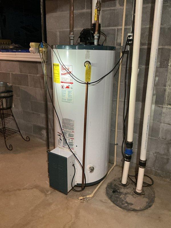 Provided estimate for water heater replacement in basement utility area. Assessed existing white cylindrical water heater with top-mounted circulator pump, copper supply piping, and electrical connections. Evaluated surrounding plumbing infrastructure including PVC drainage system, brass shutoff valves, and existing concrete floor conditions for new installation requirements.