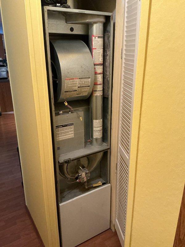 Conducted sales estimate for furnace replacement at residential property. Documented existing HVAC system located in vertical utility closet, including current furnace unit with gray metal casing and associated ductwork. Photographed existing Muller thermostat and complete equipment configuration to provide accurate replacement proposal.