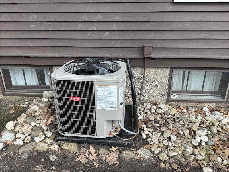 Completed installation of new furnace and added air conditioning system to existing heating-only setup. Installed Bryant 248TAN03600A condenser unit on exterior pad against foundation wall with proper clearances, positioned between basement windows on gray-sided structure. Unit installation included electrical disconnect box mounting, conduit routing along exterior wall, and connection to indoor evaporator coil. Furnace was pulled from stock and staged, while AC condenser experienced backorder delays through supplier before arrival and final installation. System positioned on concrete pad with landscaping rock surround, all electrical connections completed per code requirements. Back porch access code 6412 utilized for entry during installation process.