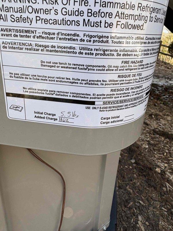 Completed full air conditioning system installation including Bryant 16.5 SEER2 condenser unit positioned on new protective pad in ground-level area beneath elevated deck. Installed new line set with proper refrigerant charge of 5.5 lbs initial plus 11 oz added charge per manufacturer specifications. Unit mounted on black equipment pad over wood chip base with lattice skirting, all connections secured and system tested for proper operation.