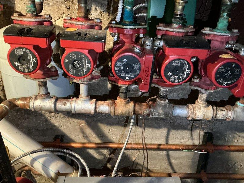 Conducted on-site evaluation of existing boiler system for replacement estimate. Documented current water heater installation with copper piping connections, pressure relief valve, and gas line configuration in basement utility area. Assessed manifold system with five circulator pumps showing significant age-related corrosion and deterioration on copper piping and fittings. Photographed equipment condition and mechanical room layout to develop comprehensive replacement proposal for aging heating distribution system.