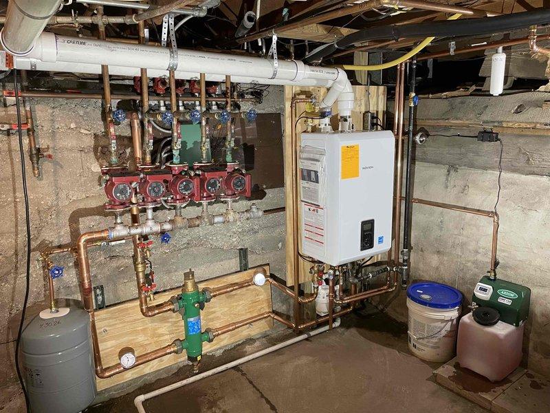 Completed full boiler replacement in basement mechanical room. Removed and disposed of existing boiler, accessories, and water heater circulation pump. Installed new Navien wall-hung combi boiler with complete copper piping connections to existing radiant heating manifold system. Installation includes new expansion tank, pressure relief valves, ball valves with pressure gauges, and proper venting through PVC exhaust system. Connected boiler to multi-zone radiant heating distribution manifold with red-handled zone valves mounted on wall board. All copper connections soldered and pressure tested. System filled, purged of air, and tested for proper operation across all heating zones. Unit secured to concrete wall per manufacturer specifications with all safety controls verified operational.