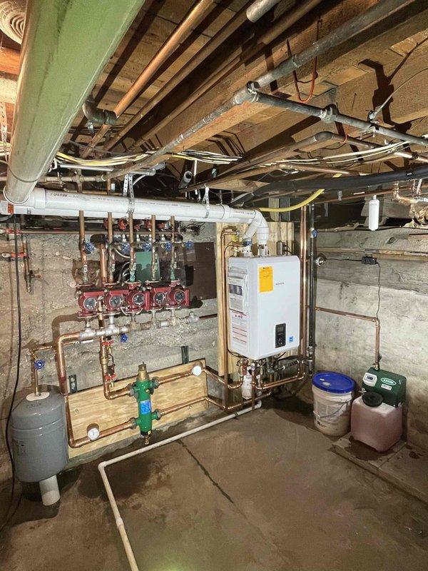 Completed full boiler replacement in basement mechanical room. Removed and disposed of existing boiler, accessories, and water heater circulation pump. Installed new Navien wall-hung combi boiler with complete copper piping connections to existing radiant heating manifold system. Installation includes new expansion tank, pressure relief valves, ball valves with pressure gauges, and proper venting through PVC exhaust system. Connected boiler to multi-zone radiant heating distribution manifold with red-handled zone valves mounted on wall board. All copper connections soldered and pressure tested. System filled, purged of air, and tested for proper operation across all heating zones. Unit secured to concrete wall per manufacturer specifications with all safety controls verified operational.