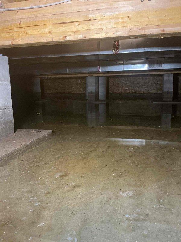 Responded to crawl space flooding at a 5-year-old residential property. Inspected furnace, water pump, and water softener for water damage following ground water intrusion; confirmed all equipment remained operational despite standing water present throughout crawl space. Documented extensive moisture on concrete floor with reflective pooling visible across multiple areas. Assessed structural supports, floor joists, and foundation for water-related damage. Photographed conditions showing damp concrete surfaces, block foundation walls, and overhead wooden joists with moisture exposure. Coordinated with HVAC technician on-site to evaluate mechanical systems. Recommended permanent water mitigation solution to prevent future flooding incidents and protect mechanical equipment from potential damage.