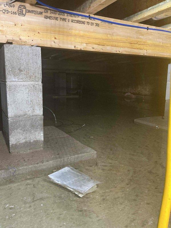 Responded to crawl space flooding at a 5-year-old residential property. Inspected furnace, water pump, and water softener for water damage following ground water intrusion; confirmed all equipment remained operational despite standing water present throughout crawl space. Documented extensive moisture on concrete floor with reflective pooling visible across multiple areas. Assessed structural supports, floor joists, and foundation for water-related damage. Photographed conditions showing damp concrete surfaces, block foundation walls, and overhead wooden joists with moisture exposure. Coordinated with HVAC technician on-site to evaluate mechanical systems. Recommended permanent water mitigation solution to prevent future flooding incidents and protect mechanical equipment from potential damage.
