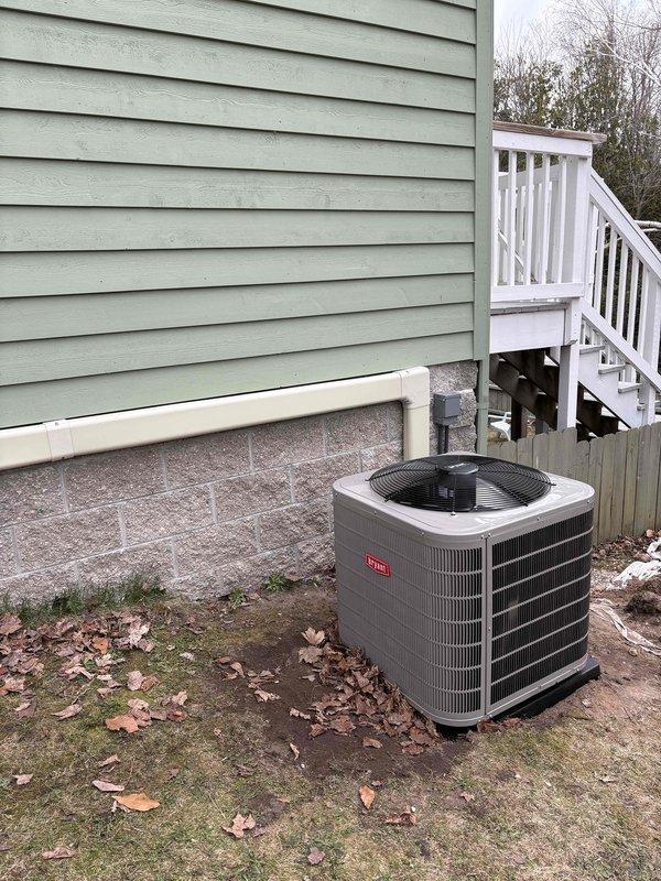 Completed full HVAC system replacement including outdoor condensing unit and indoor air handler components. Installed new Armstrong Air furnace system in basement mechanical room with properly configured PVC exhaust and intake venting. Positioned gray cylindrical outdoor AC condenser unit on concrete pad adjacent to residential structure with adequate clearance from building siding and nearby stairway. Connected all refrigerant lines, electrical components, and drainage systems per manufacturer specifications. Verified proper operation of both indoor and outdoor equipment, confirmed airflow through ductwork, and ensured all safety labels and warning placards remain visible and intact.