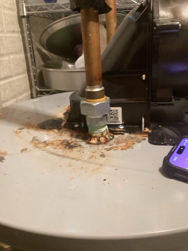 Responded to water heater leak in drain pan. Upon inspection, found significant corrosion and rust accumulation at copper pipe union connection above unit, with evidence of active water seepage causing rust staining on surrounding surfaces. Verified unit is a 4-year-old American-brand water heater showing advanced corrosion on exterior panels and pipe connections. Documented extensive rust streaking on unit casing and deteriorated pipe fittings. Verified warranty coverage and photographed conditions for warranty claim processing.