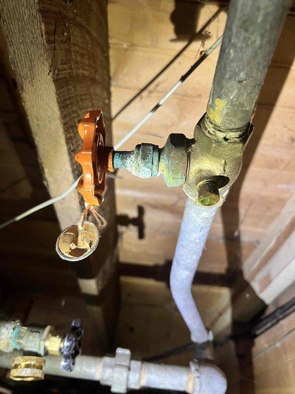 # Plumbing Leak Repair - Main Level Tub and Toilet Supply Valve

Responded to report of main level bathtub leaking into basement and toilet supply valve leak in blue bathroom. Upon arrival, accessed property through unlocked front door as instructed.

Inspected basement area beneath main level tub and identified active leak dripping through floor joists. Found makeshift towel placed under leak point to catch water. Traced leak source to deteriorated drain assembly connections above. Examined exposed copper supply lines and drain piping in basement ceiling, noting significant corrosion and verdigris buildup on copper pipes at joint connections. Documented extensive oxidation on aged copper piping and fittings, indicating long-term moisture exposure and material degradation.

Inspected blue bathroom toilet supply valve and confirmed active leak at valve connection point. Evaluated condition of existing shut-off valve and supply line. Assessed surrounding plumbing infrastructure including