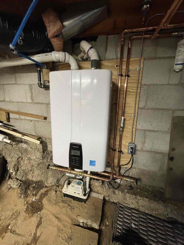Completed installation of Bryant furnace system with add-on air conditioning components in basement utility area. Installed Energy Star certified tankless water heater on concrete block wall with proper copper supply lines, PVC venting system, and gas piping as specified. Connected black insulated flex ductwork to furnace unit, secured to floor joists, and integrated evaporator coil assembly with condensate management system for complete HVAC operation.