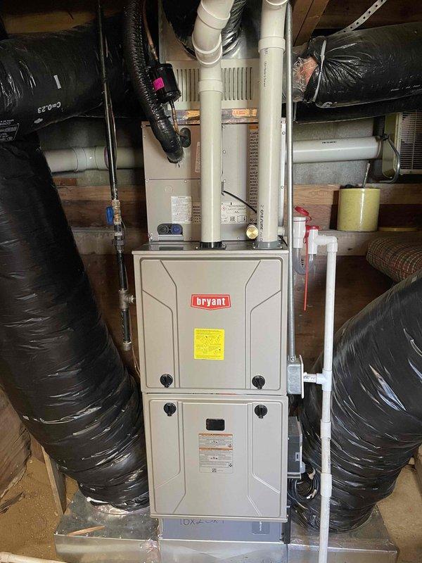 Completed installation of Bryant furnace system with add-on air conditioning components in basement utility area. Installed Energy Star certified tankless water heater on concrete block wall with proper copper supply lines, PVC venting system, and gas piping as specified. Connected black insulated flex ductwork to furnace unit, secured to floor joists, and integrated evaporator coil assembly with condensate management system for complete HVAC operation.