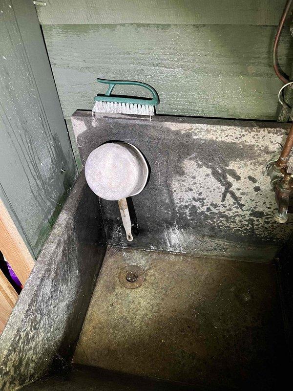 Completed annual spring turn-on service for cottage property. Restored water supply to exterior utility sink station featuring three brass faucets and dual concrete basins, connecting hoses and testing all fixtures for proper operation. Addressed exterior porch area cleaning needs, removing accumulated debris and moisture staining from concrete surfaces using scrub brush to prepare space for seasonal use.