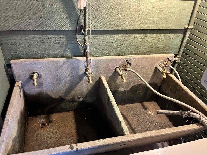 Completed annual spring turn-on service for cottage property. Restored water supply to exterior utility sink station featuring three brass faucets and dual concrete basins, connecting hoses and testing all fixtures for proper operation. Addressed exterior porch area cleaning needs, removing accumulated debris and moisture staining from concrete surfaces using scrub brush to prepare space for seasonal use.