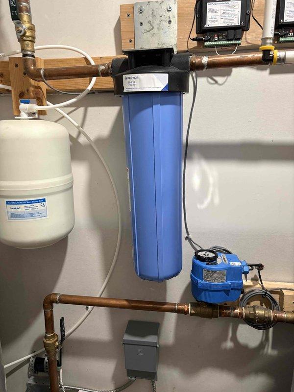 Responded to service call to evaluate residential HVAC system for potential serviceability. Upon arrival, conducted thorough assessment of outdoor air conditioning condenser unit and associated indoor mechanical systems. The outdoor unit, a residential AC condenser with beige metal casing, was found properly mounted on base pad with gravel foundation and appropriate electrical disconnect boxes installed per code requirements.

Interior inspection revealed a complex water treatment and hydronic heating system including whole-house water filtration with blue cylindrical filter housing, white expansion tank, and electric circulator pump integrated into copper piping network. All components appeared to be functioning within normal parameters with proper mounting and connections. Electrical monitoring equipment and control panel were observed in good working condition.

Documented system configuration with photographs for reference and determined that while the installation is more complex 