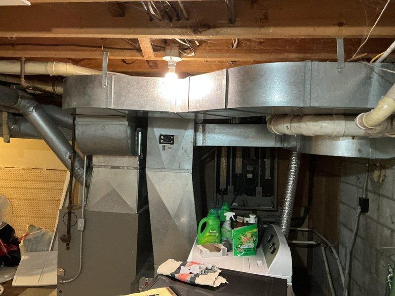 Conducted on-site assessment for furnace upgrade to accommodate dual-fuel capability (wood and propane). Inspected existing HVAC system in basement, documented current equipment configuration including ductwork layout and electrical service panel with 200-amp disconnect switch showing significant age and corrosion. Photographed existing furnace installation, surrounding infrastructure, and electrical components to prepare comprehensive quote for dual-fuel conversion system.