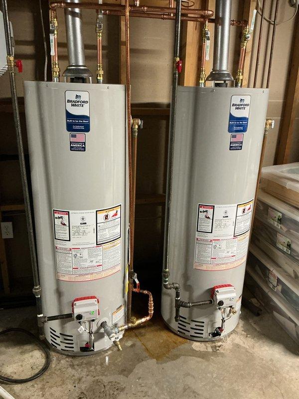 Technician responded to a water heater leak in a residential utility room where two propane water heaters were previously installed in series configuration. The left unit exhibited active leaking from the top connection, causing water accumulation on the concrete floor. After testing the right unit and confirming proper ignition and operation, both existing water heaters were removed and replaced with two Bradford White 40-gallon professional-grade atmospheric vent propane models. The new units were reconfigured from series to parallel plumbing arrangement with individual shut-off valves installed for each water heater, providing independent isolation capability. All copper supply lines were connected with brass compression fittings, and proper venting was established for both units. System was tested, fired successfully, and left in full operational condition with no leaks detected.