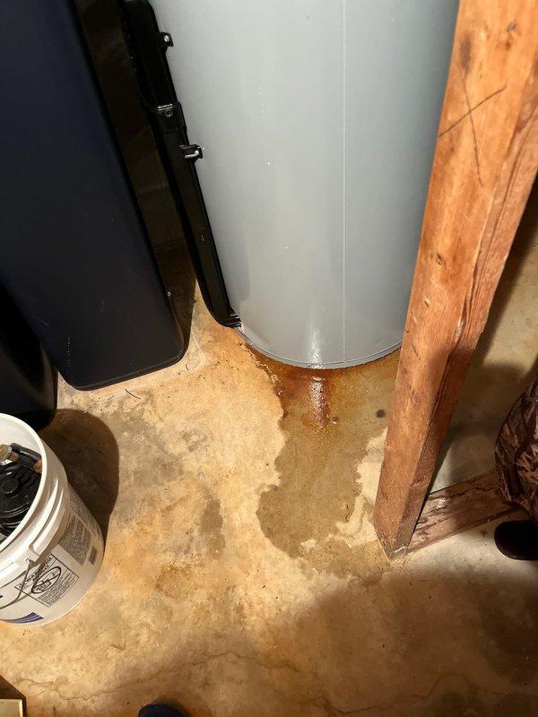 Responded to water heater leak reported at base of unit. Upon arrival, confirmed active leakage from bottom of American-brand water heater with extensive water staining and rust-colored corrosion visible on tank base and surrounding concrete floor. Unit still under manufacturer warranty. Documented damage with photos showing compromised tank integrity and water damage to utility room floor. Recommended warranty replacement due to tank failure.