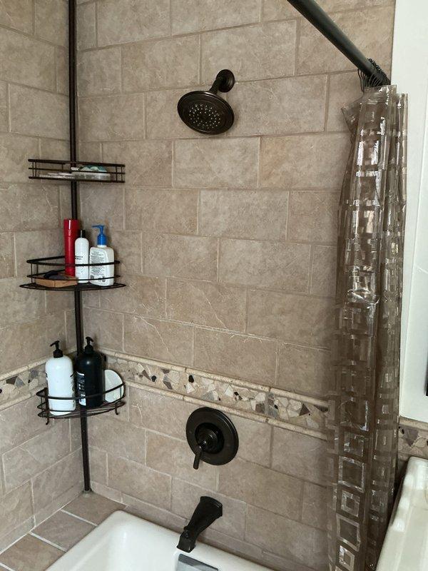 Responded to customer complaint of discolored water from hot water supply. Upon arrival, inspected 10-year-old water heater and confirmed discoloration issue. Documented existing shower fixtures and plumbing system with photographs showing bronze-finished showerhead, control valves, and tub spout with beige tile surround. Based on age of unit and water quality concerns, discussed replacement options with customer for aging water heater system.